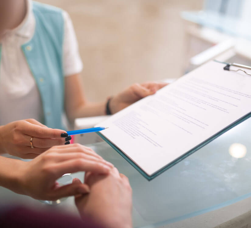 Healthcare professional holding clipboard with pen, reviewing patient form at dental office desk.