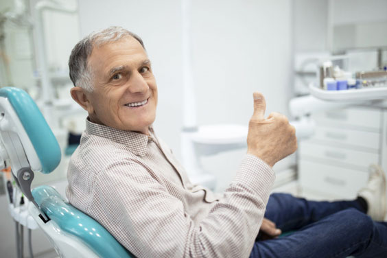 Middle-aged man giving thumbs up in dental chair at modern dental office.