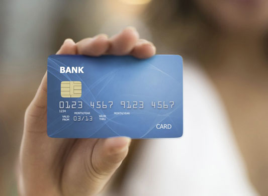Person holding blue bank credit card with chip and card number visible.