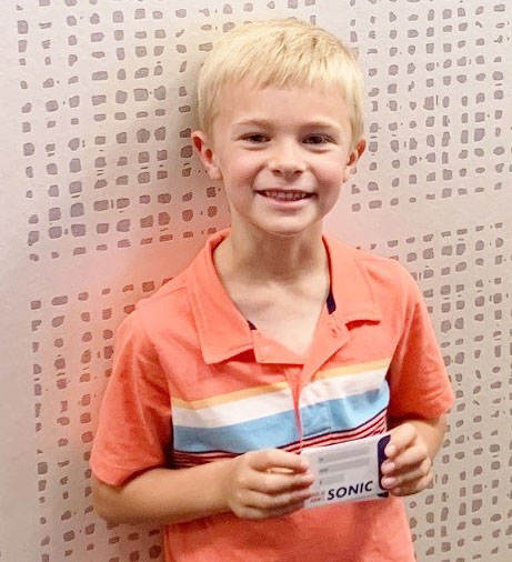 Young boy smiling at camera wearing orange shirt in dental office setting.