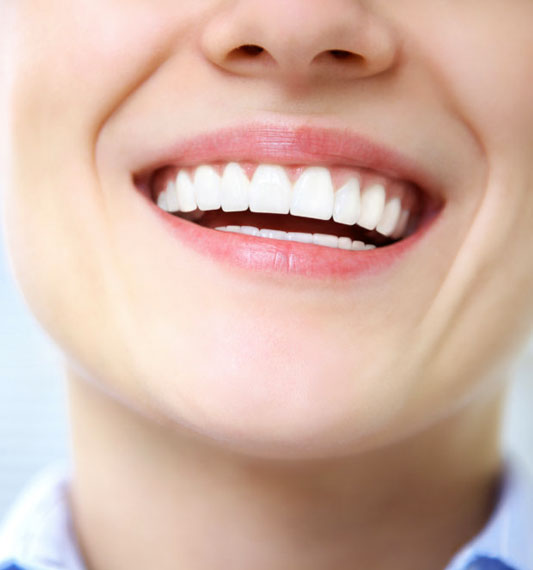 Close-up of person smiling, displaying bright white healthy teeth and pink lips against light background.