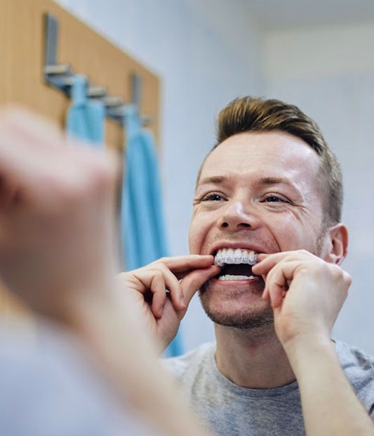 Man flossing teeth in bathroom mirror with towel in background.