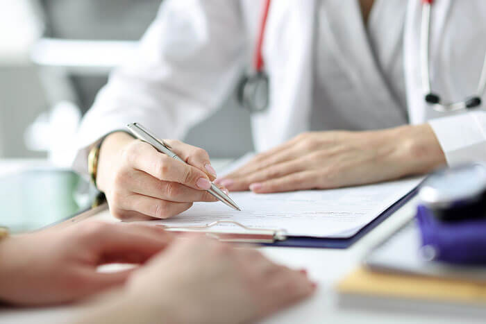Doctor in white coat writing on clipboard while patient extends hand in dental office setting.