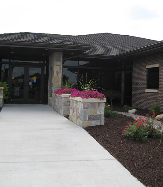Modern brick dental office building with concrete driveway and pink flowering planters at entrance.