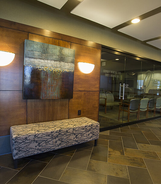 Modern dental office reception area with granite counter, wood paneling, and contemporary artwork.