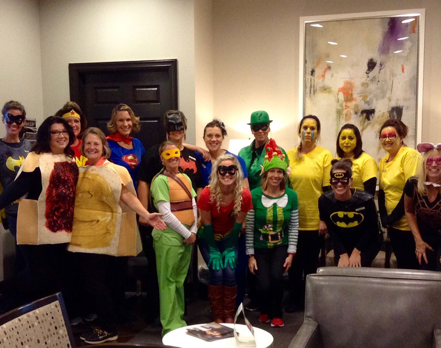Dental office staff wearing colorful costumes gathered together for a group photo in clinic interior.