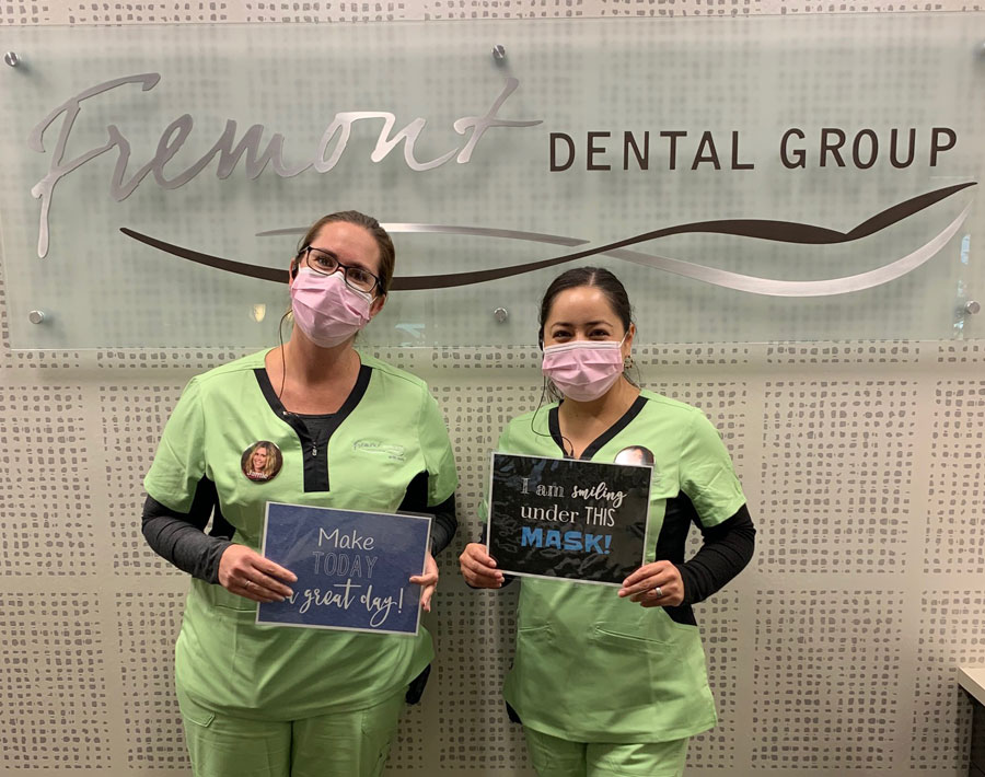 Two dental professionals in green scrubs holding chalkboards at Fremont Dental Group office