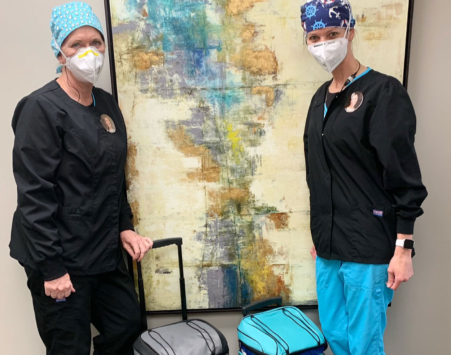 Two masked dental professionals stand beside an abstract artwork in a clinical office setting.