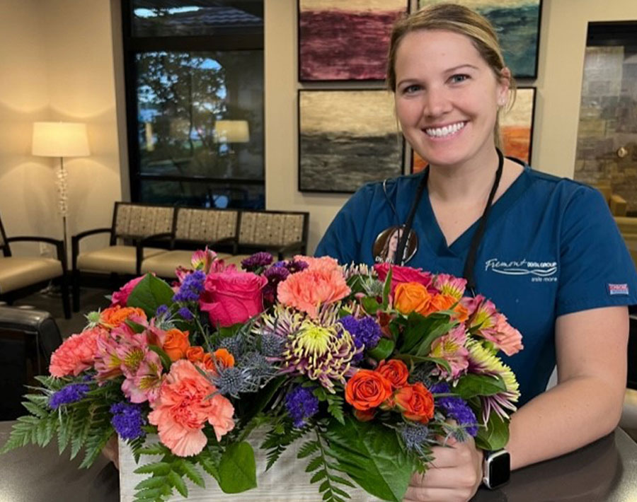 Dental staff member holding colorful flower arrangement in modern dental office reception area.