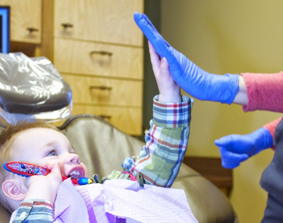 Baby wearing purple bib during dental examination with dentist's gloved hands visible in clinical setting.