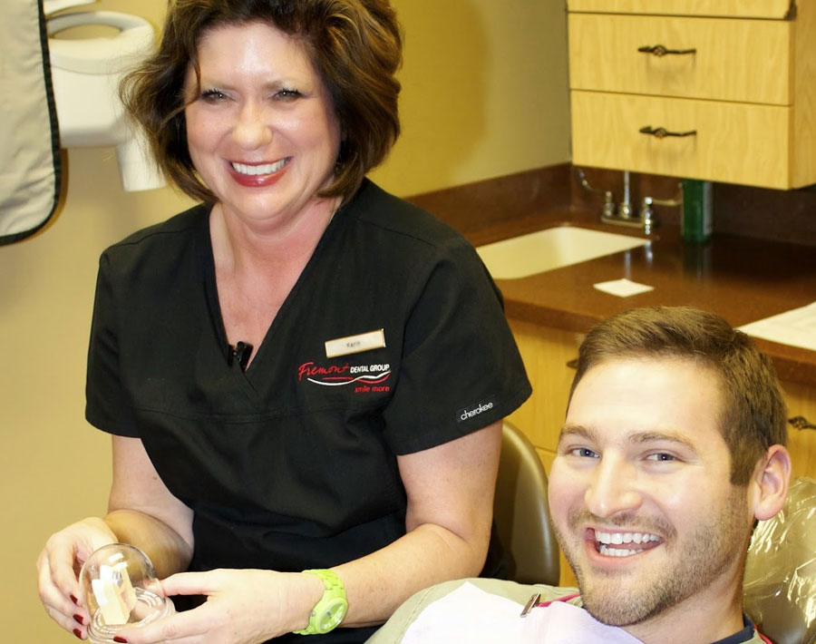 Dental hygienist in black scrubs assists male patient at Fremont Dental Group office.