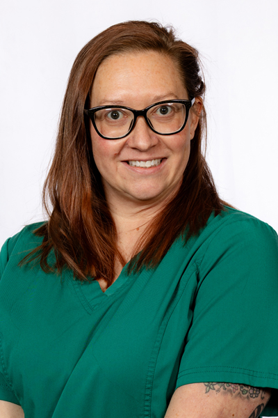 Woman wearing green scrubs and glasses smiling at camera in professional dental office portrait.