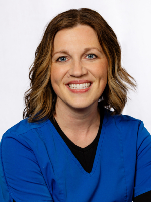 Professional headshot of smiling woman in blue cardigan against white background for dental practice.