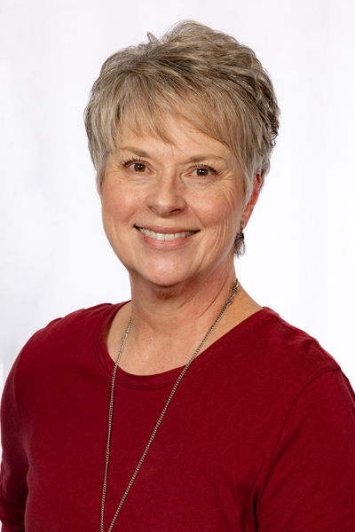 Smiling woman with short gray hair wearing maroon top in professional headshot for dental practice.