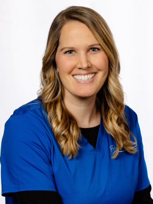 Professional headshot of smiling woman in blue scrubs against white background, dental practice staff portrait.