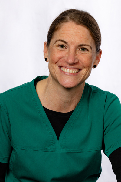 Woman in green dental scrubs smiling at camera against white background.