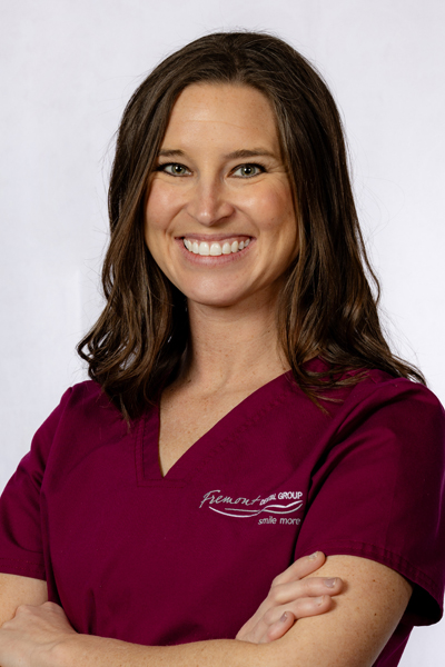 Professional headshot of female dental staff member in maroon scrubs smiling at camera, indoor clinical setting.