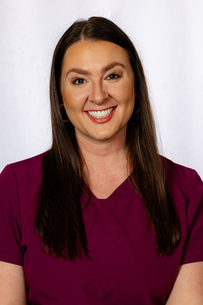 Professional headshot of woman with long dark hair wearing maroon top, smiling at camera against white background.