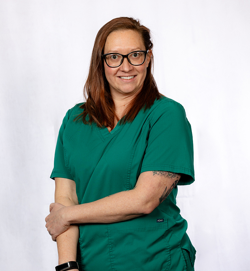 Female dental professional in green scrubs smiling at camera against white background.