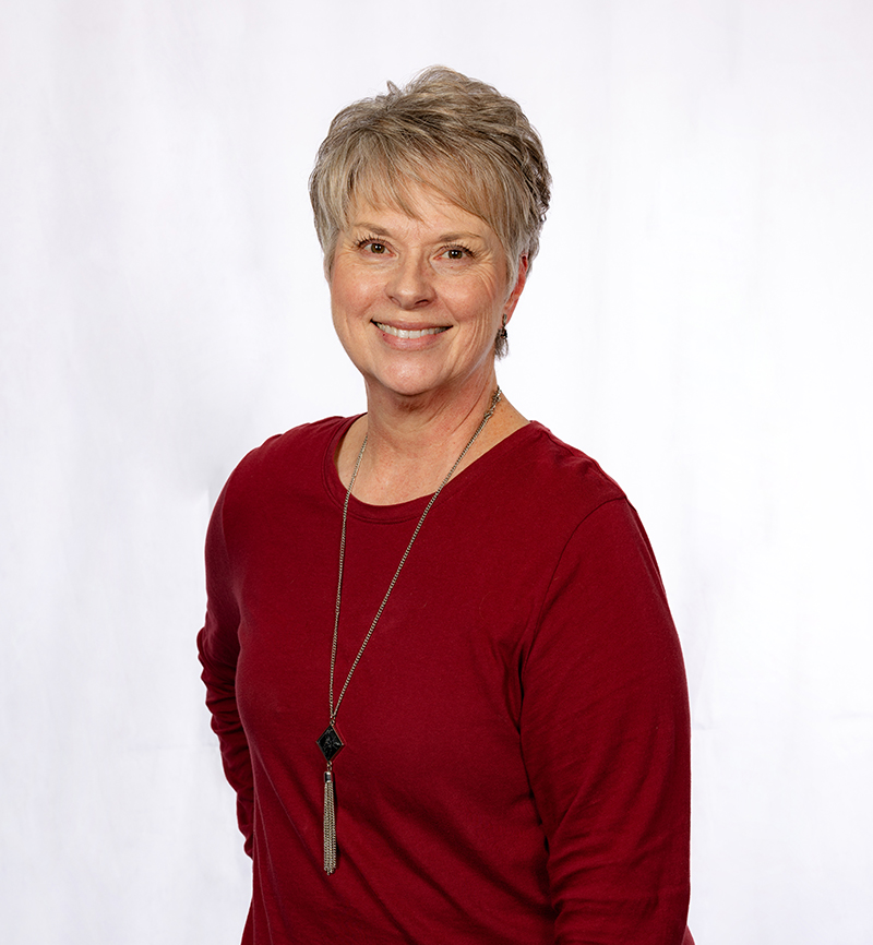 Professional headshot of a woman with short blonde hair wearing a red top against a white background.