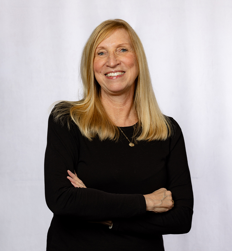 Professional woman in black blazer smiling with arms crossed against white background.