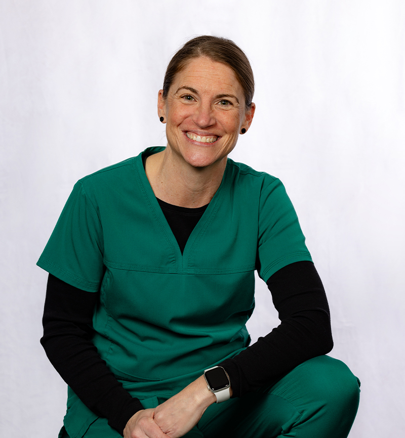 Smiling dental professional in green scrubs posing against white background.