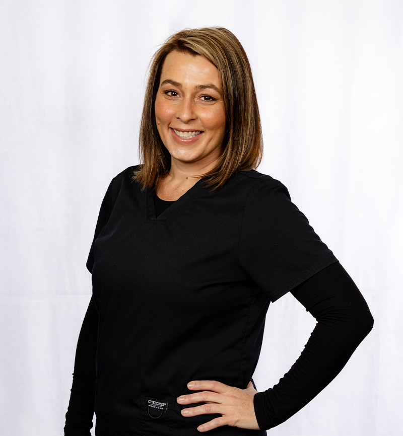 Professional headshot of woman in black long-sleeve shirt against white background for dental practice.