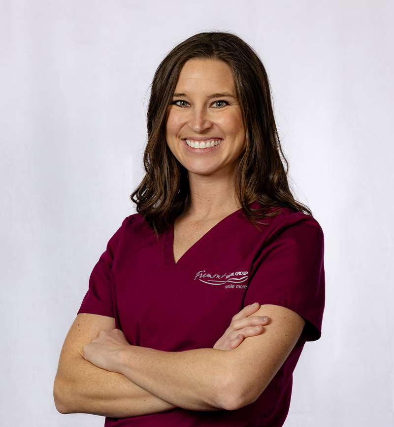 Professional woman in maroon scrubs smiling with arms crossed against white background.
