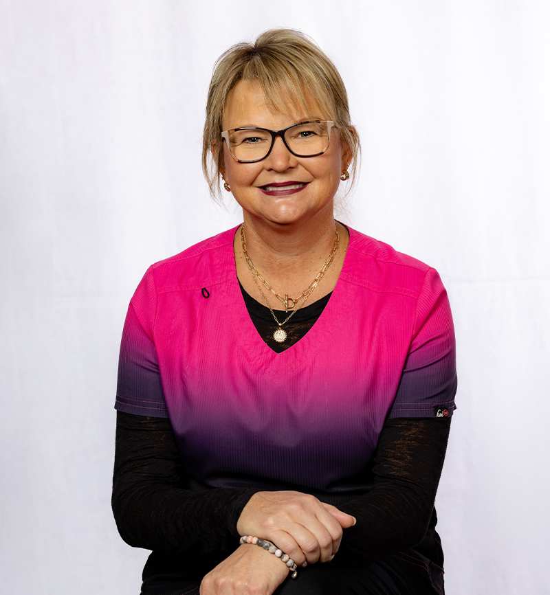 Woman wearing glasses and pink-to-black ombre top smiles at camera in professional headshot.