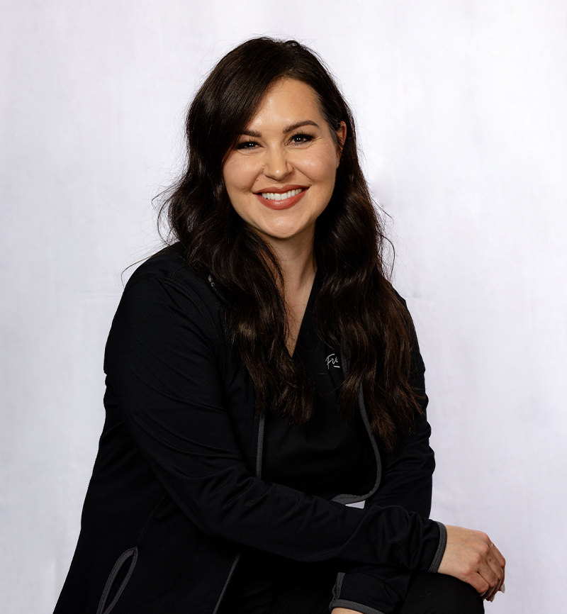Professional headshot of a woman in black blazer smiling against white background.