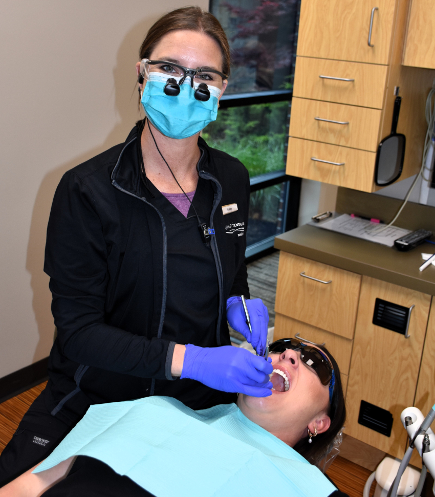 Dentist in protective gear examining patient in dental treatment chair.