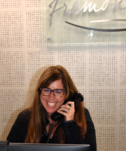 Woman with glasses smiling while on phone call at dental office desk.