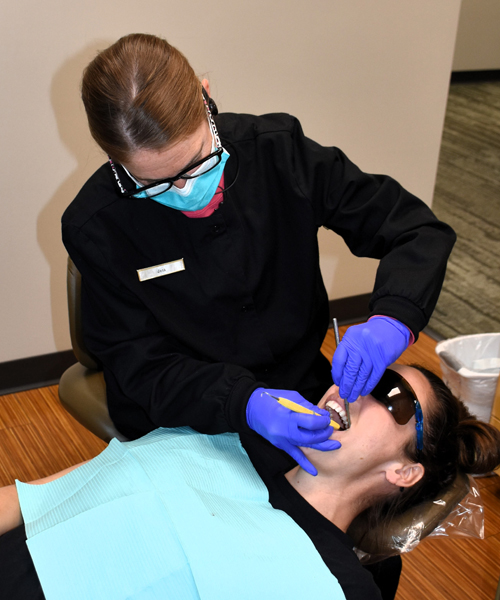 Dental hygienist in blue gloves examining patient's teeth in clinical setting.