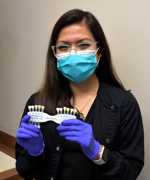Dental professional wearing mask and gloves holding teeth model in clinical setting.