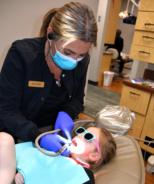 Dentist in blue mask and gloves examining child patient's teeth in dental office.