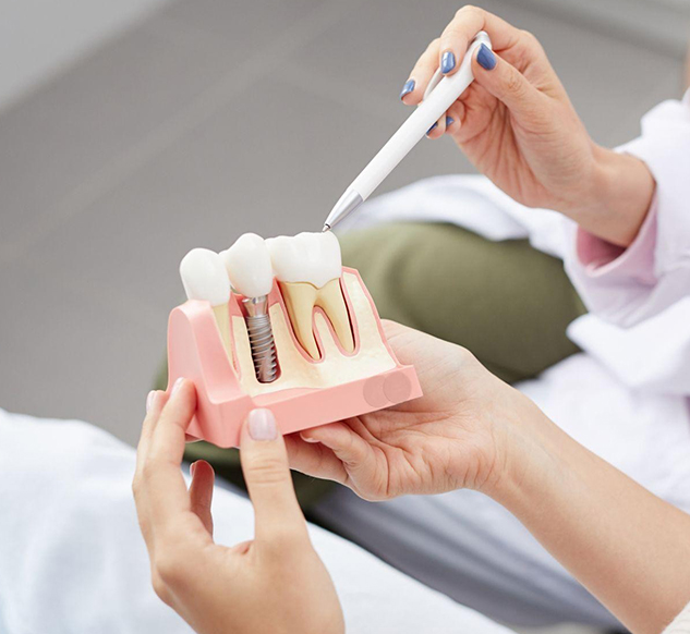 Dentist demonstrating dental implant components and model to patient in clinical setting.