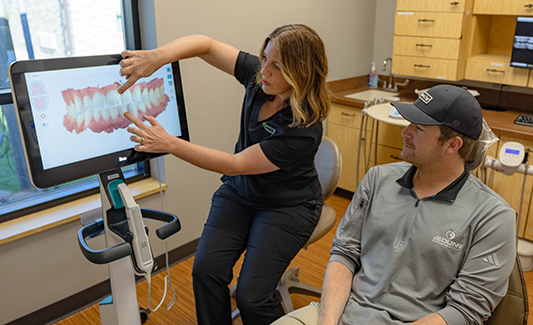 Dental professional demonstrates tooth model on screen to patient in modern dental office.