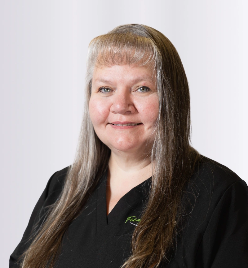 Professional headshot of woman with long hair wearing black shirt against white background at dental office.