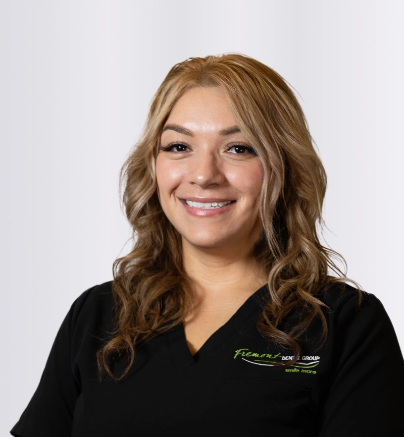 Professional headshot of smiling woman in black Fremont Dental scrubs against white background.