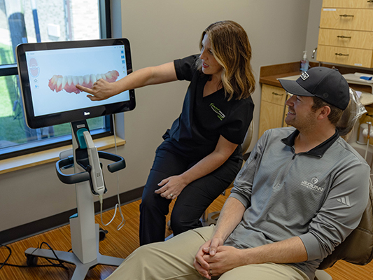 Dental professional pointing at digital screen while consulting with male patient in dental office.