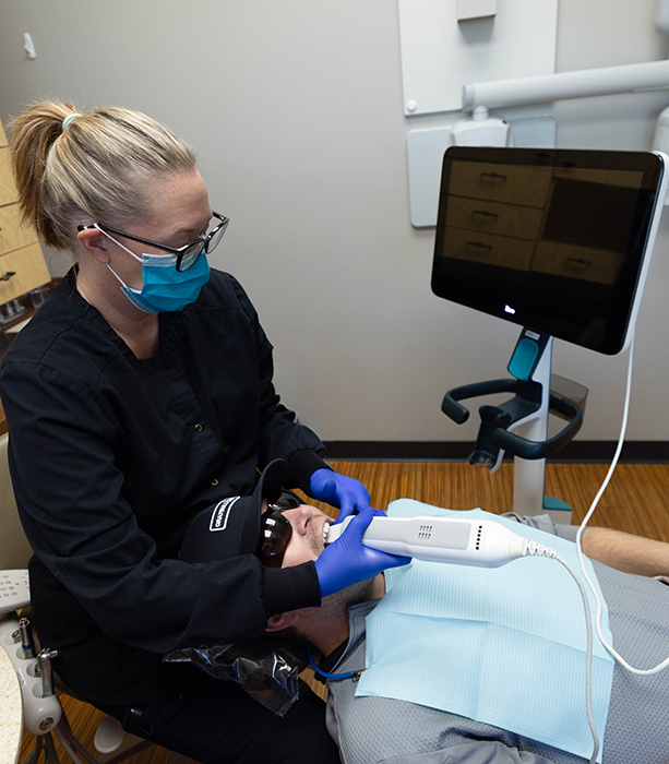 Dental hygienist in blue gloves examines patient's teeth during routine checkup at Fremont Dental Group.