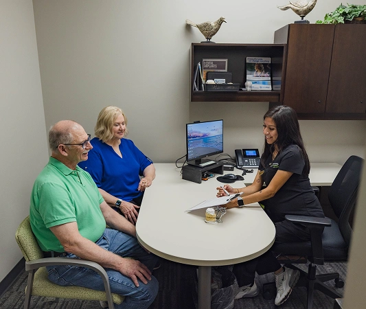 Two patients consult with female dental professional at round table in modern dental office.