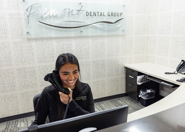 Dental receptionist at front desk in Fremont Dental Group office wearing black scrubs.