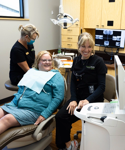 Young patient in dental chair with two dental professionals in modern dental office treatment room.
