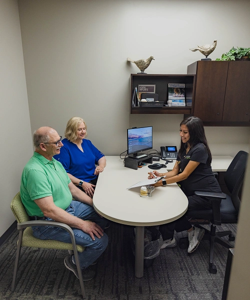 Three people in dental office consultation around white table with laptop and documents.