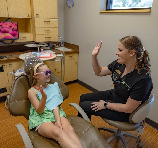 Pediatric dentist demonstrating proper tooth brushing technique to young patient in dental office.