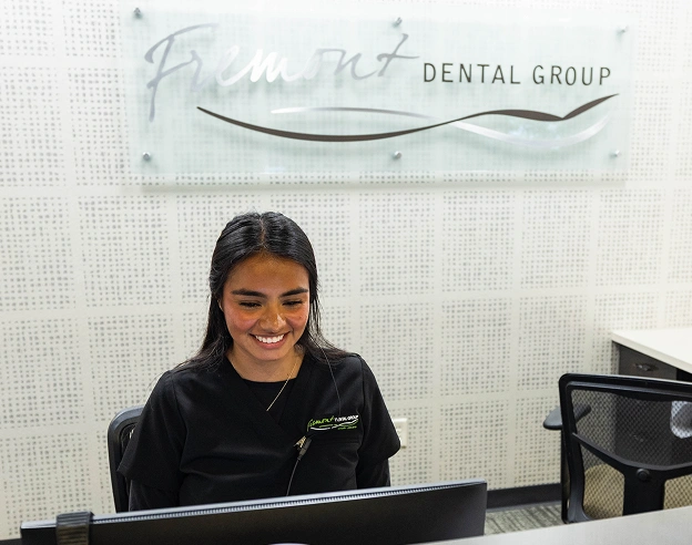 Smiling receptionist at Fremont Dental Group front desk wearing black uniform.