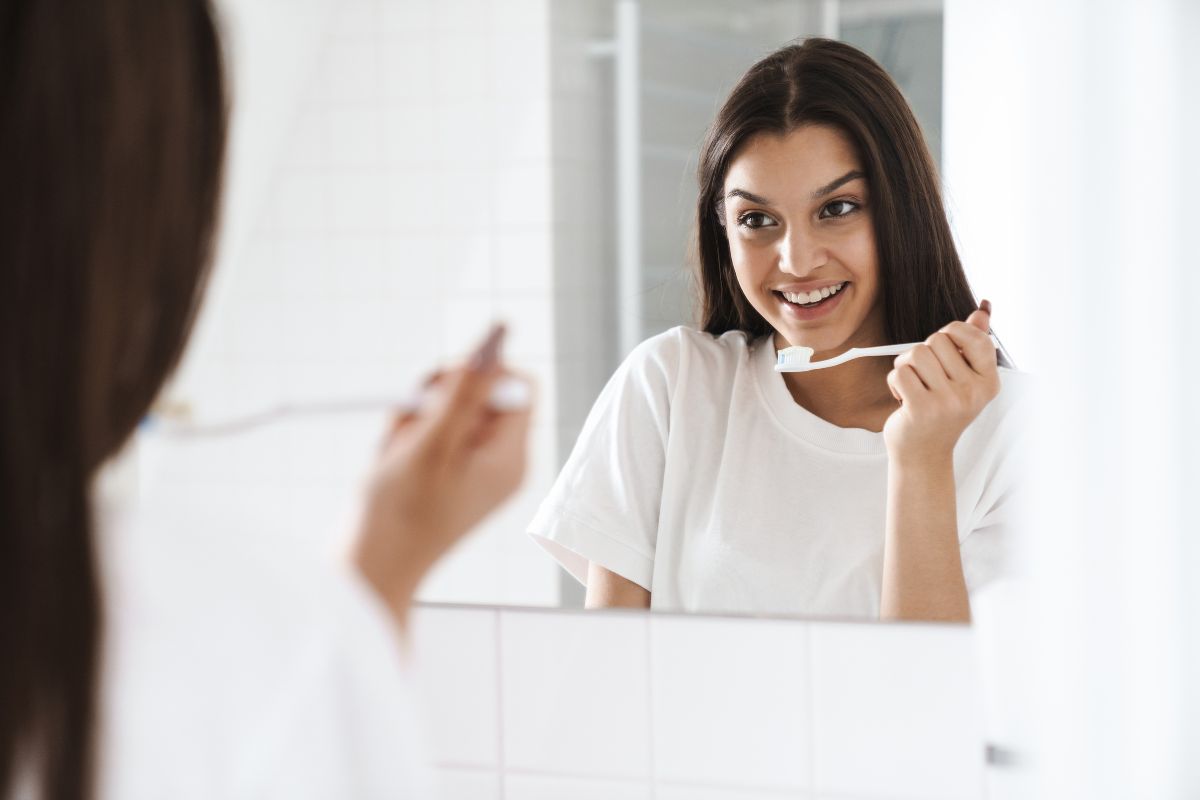 Person brushing teeth in front of a mirror as part of a daily oral hygiene routine for a healthy smile.